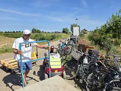 Een vrijwilliger loopt met een steekwagen langs de rij opknapfietsen en een scootmobiel